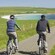 Two bicycle riders riding throught he countryside toward a coastal inlet